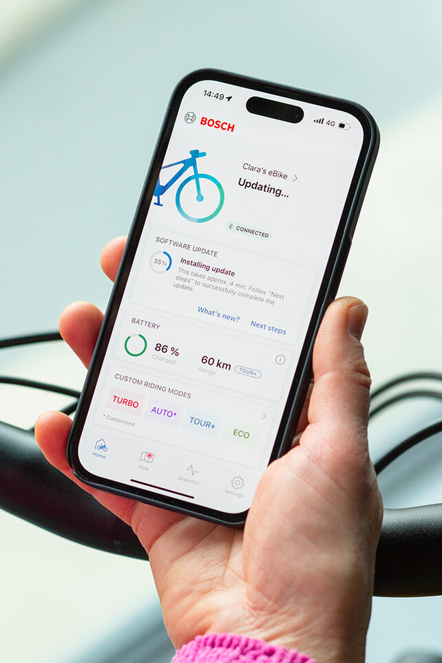 Een persoon houdt een smartphone dichtbij zijn eBike en installeert updates op de smartphone-app.