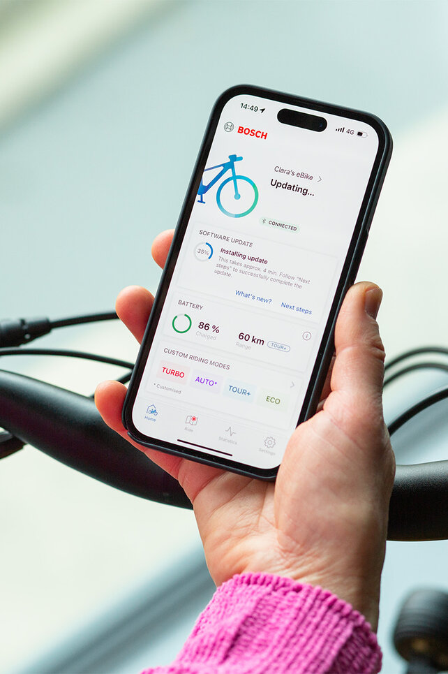 A person holds a smartphone near their eBike and installs updates using the smartphone app.