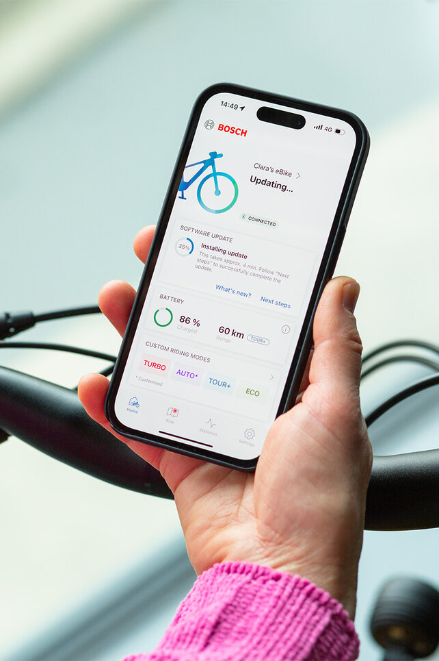 A person holds a smartphone near their eBike and installs updates using the smartphone app.