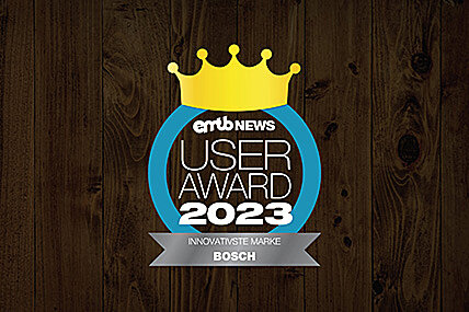 Icon with the text "emtb NEWS USER AWARD 2023": A golden crown above the text, enclosed by a blue circle. Below it reads "MOST INNOVATIVE BRAND BOSCH". The background has a dark wood finish.