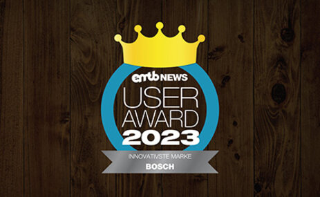Icon mit dem Text „emtb NEWS USER AWARD 2023“: Eine goldene Krone über der Schrift, umrandet von einem blauen Kreis. Unten steht „INNOVATIVSTE MARKE BOSCH“. Der Hintergrund ist aus dunklem Holz.