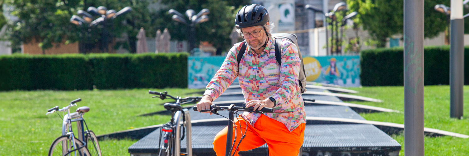 Ein bunt gekleideter Mann fährt in städtischer Umgebung ein eBike.