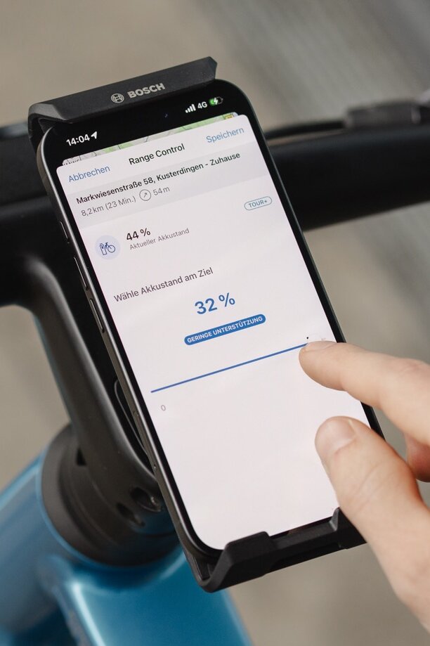 Nahaufnahme eines Smartphones, das die Funktion Range Control in der eBike Flow App zeigt. Ein Nutzer stellt über einen Schieberegler den gewünschten Akkustand bei der Ankunft am Ziel auf 32 Prozent ein, um die Reichweite für die geplante Route zu optimieren.