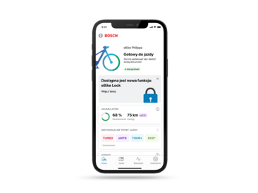 Smartphone wyeksponowany na szarym tle. Display pokazuje stronę Home w otwartej eBike Flow App.