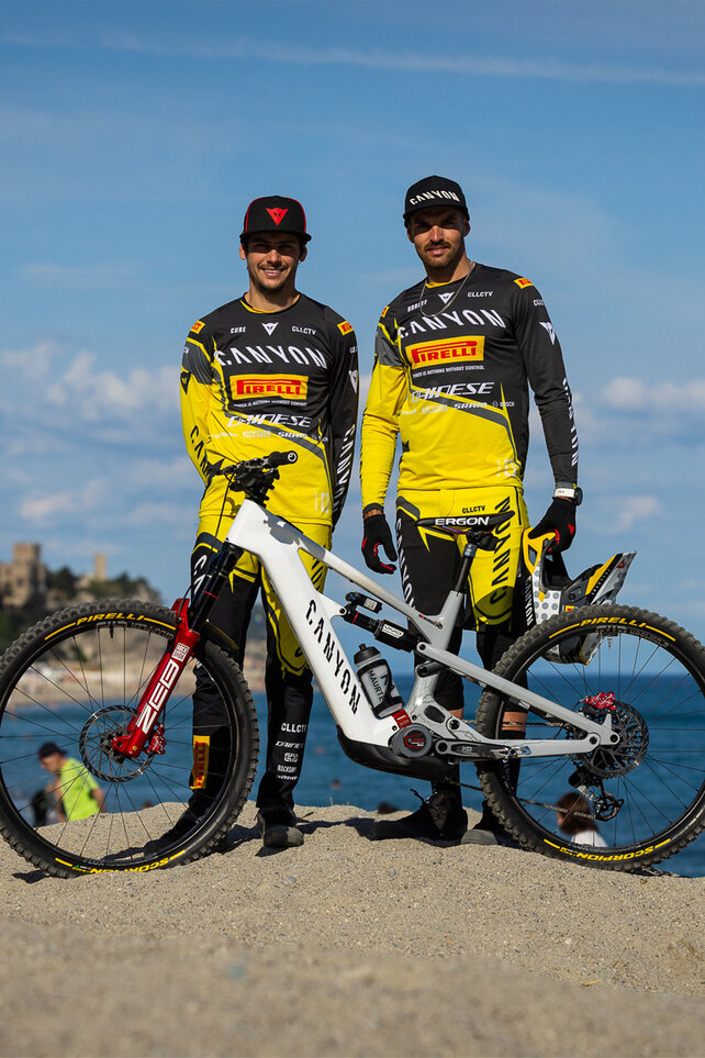 Jose Borges and Alex Cure from the Canyon Collective Factory Enduro Racing Team are pictured with an eBike on a beach.