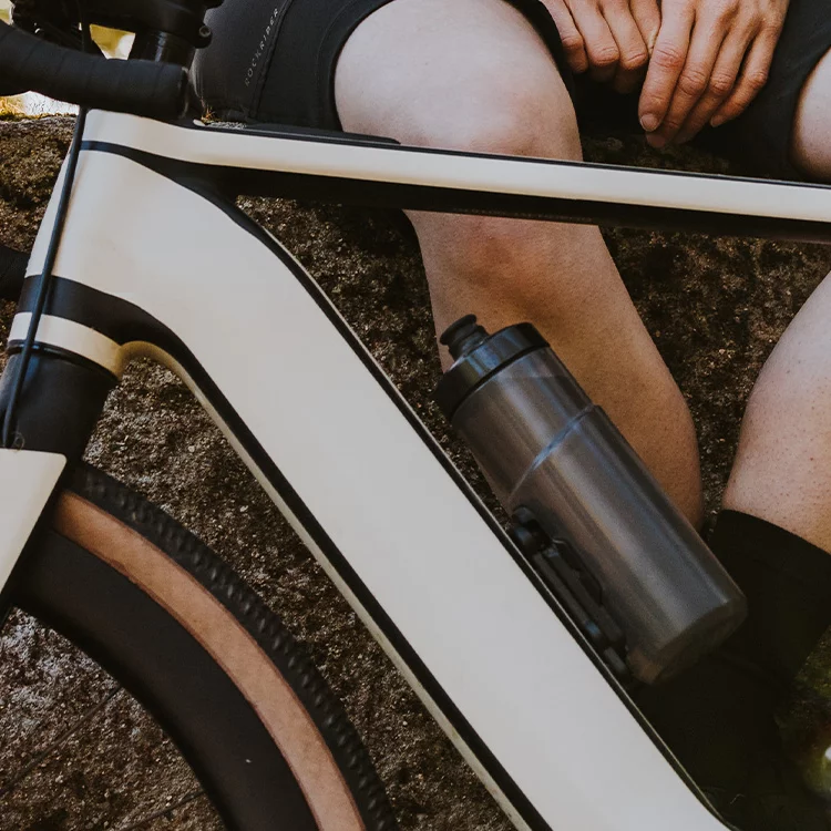 Nahaufnahme eines eBikes. Zu sehen ist der obere Teil des Rahmens mit einer angebrachten Trinkflasche. Im Hintergrund sitzt jemand auf einer Mauer.