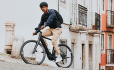 eBike rider drives up a mountain, you can see buildings in the background.