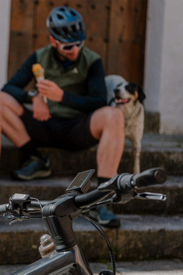 Eine Frau und ein Mann mit Helmen essen Eis auf einer Treppe. Vor ihnen parken ihre eBikes.