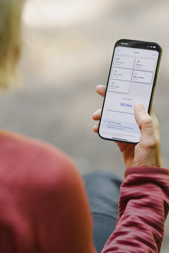 Un regard par-dessus l’épaule d’une femme qui règle individuellement les valeurs de performance dans l’application eBike Flow.