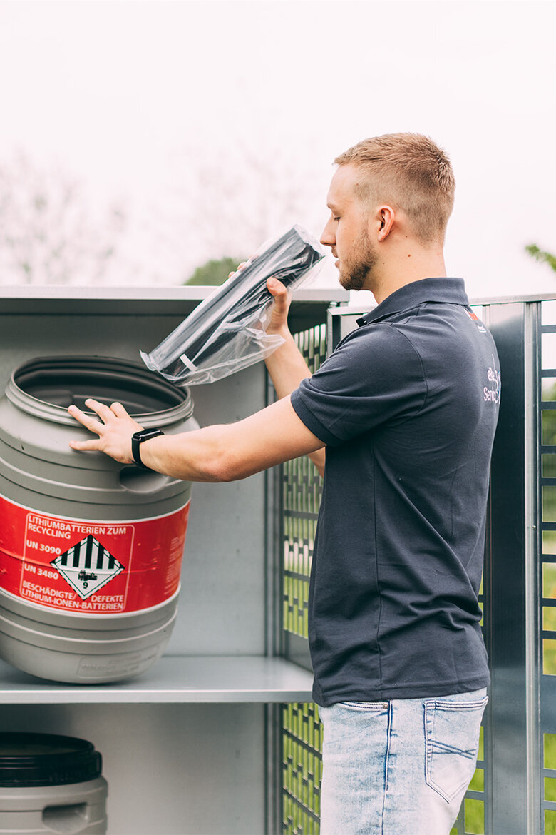 Ein Bosch Service Mitarbeiter entsorgt einen eBike Akku vorschriftsgerecht in einem Behälter, auf welchem mit rotem Warnlabel 'Lithiumbatterien zum Recycling UN 3090 UN 3480 Beschädigte/Defekte Lithium-Ionen-Batterien' steht.