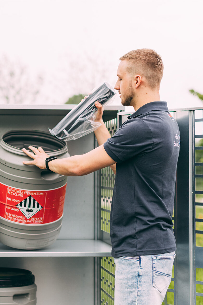 Ein Bosch Service Mitarbeiter entsorgt einen eBike Akku vorschriftsgerecht in einem Behälter, auf welchem mit rotem Warnlabel 'Lithiumbatterien zum Recycling UN 3090 UN 3480 Beschädigte/Defekte Lithium-Ionen-Batterien' steht.