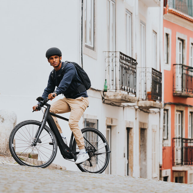Een man rijdt met zijn eBike door een straat in een stad. Op de achtergrond zie je kleurrijke huizen.